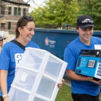 Two volunteers smiling as they carrying items for arriving student